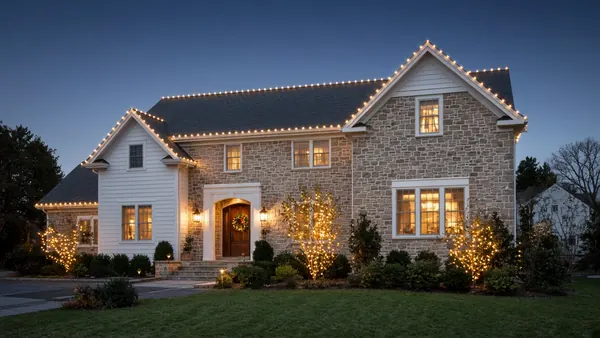 Christmas light installation: warm white lights along a home's roofline and front entry at dusk